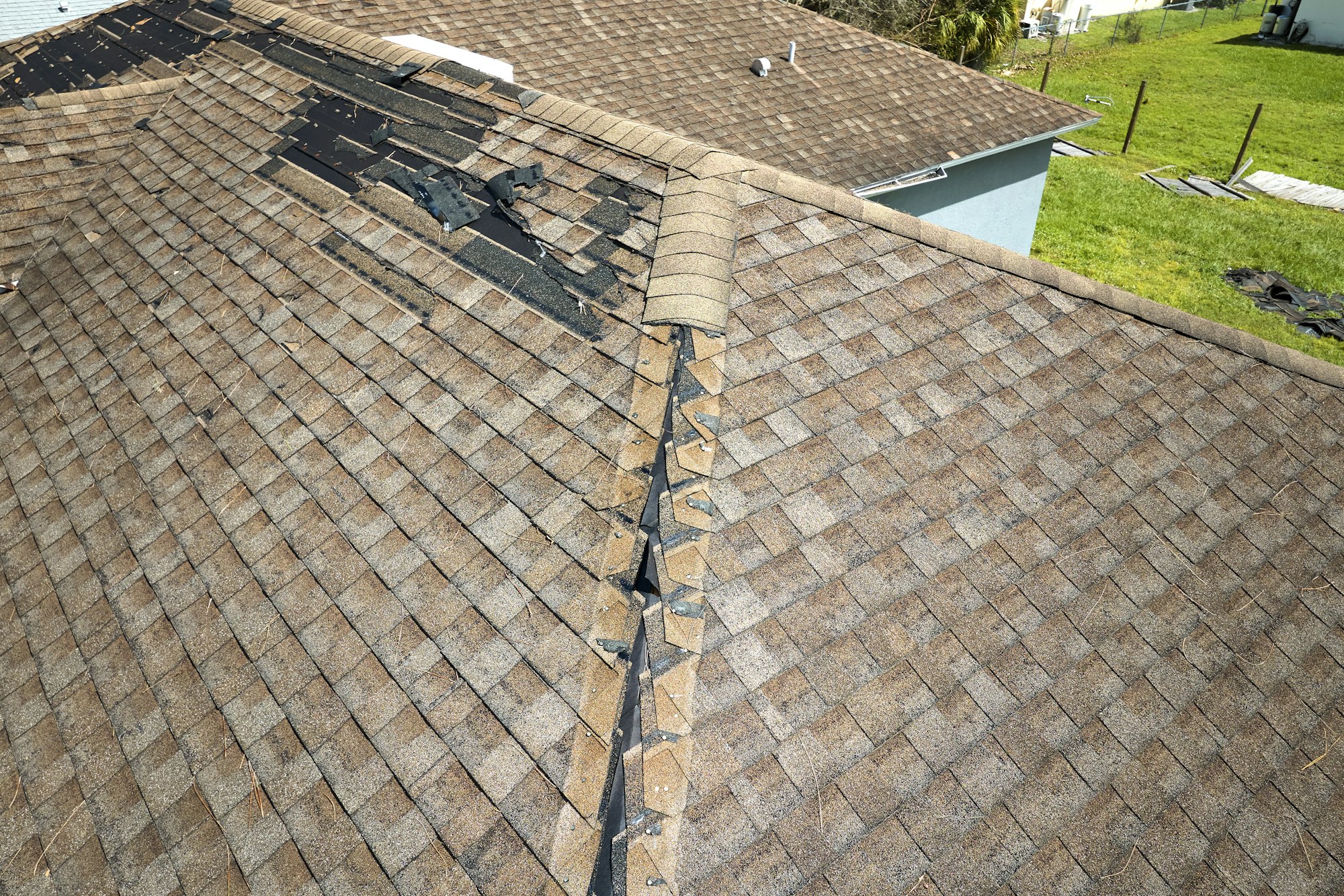 Damaged house roof with missing shingles after hurricane Ian in Florida.